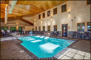 Indoor heated pool and spa area with wood-beamed ceiling and lounge seating