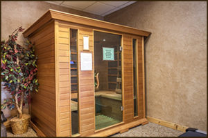 Wooden indoor sauna with glass door and bench seating in a tiled recreation area.